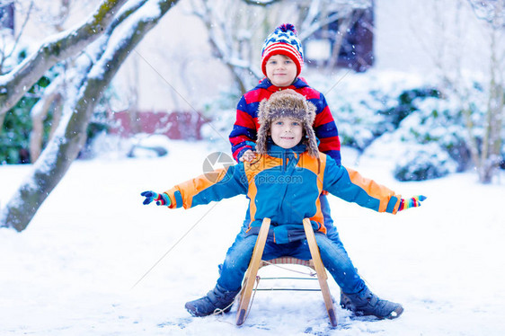 两个男孩在降雪期间享受乘坐雪橇孩子们在雪地上拉雪橇兄弟姐妹骑着雪橇双胞胎在户外玩耍朋友们在白雪皑的冬季公园拉雪橇家庭圣诞假图片