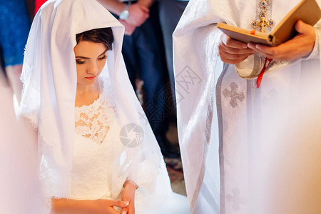 美丽的黑发新娘在白婚纱披肩下祷告图片