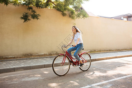 穿着牛仔裤的年轻女士在城市街道上骑红色自行车时玩得开心的肖像图片