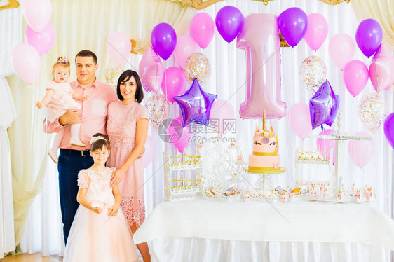 该家庭在一个带有蛋糕和充气球的节日装饰房庆祝孩子生日图片