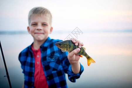 年轻金发男孩的肖像骄傲地微笑着抱着一只游鱼并展示给摄像头以对图片