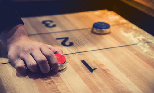 老式洗牌棋盘游戏与红色和蓝色圆盘和手拿着红色蓝圆盘在木制洗牌桌上具有选择焦点的背景图片