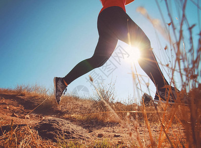 女慢跑者在日出或日落时在一座草山上冲刺图片