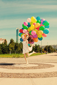 反对天空的生日快乐女人手里拿着彩虹色的气球城市街道的阳光和正能量城市草地上的背景图片