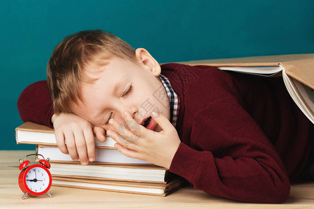 疲倦的小学生在书本上睡着了睡在课本上的小学生穿着校服的孩子躺在桌子上图片