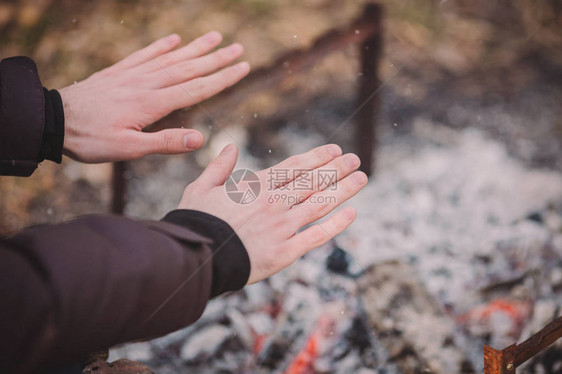 旅行者在户外的篝火旁暖手背景上的铝杯中的茶或咖啡露营细节图片