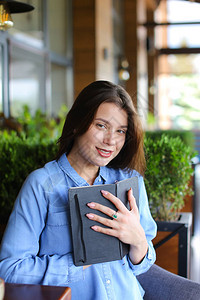 漂亮的女孩在咖啡馆里读黑色日记并摇晃着头发女穿牛仔裤衬衫午餐后在餐图片