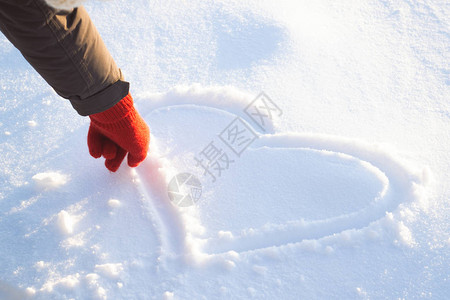 戴红手套的女手在雪地上画心冬天的概念图片