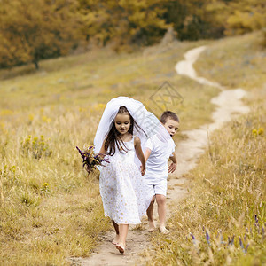年轻的新娘和新郎在户外玩婚礼夏天孩子们喜欢新婚夫妇新娘白色礼服和新娘面纱的小女孩和她的小男孩新郎一起散步背景图片