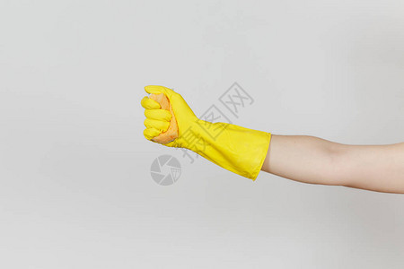 戴黄色手套的女手的特写握住并挤压黄橙色海绵图片