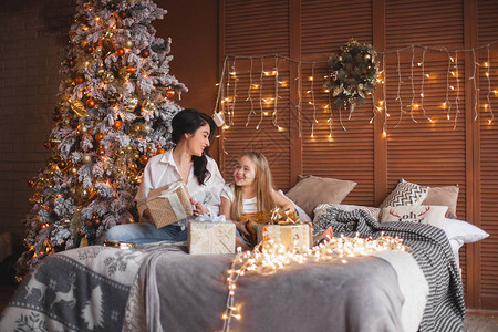 年轻母亲和女儿在床上开圣诞礼物的年图片