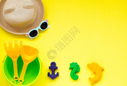 儿童玩具在黄色背景的沙子上配戴帽子和眼镜图片