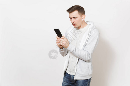 穿T恤和带耳机的轻运动衫的英俊青年学生在白色背景工作室里看电话图片