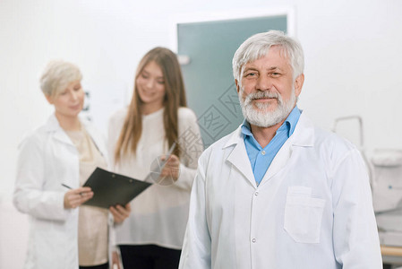 自信的老医生站在助手和病人面前图片