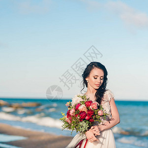 漂亮的新娘在海边的豪华婚纱礼服与花束的特写肖像海边的婚礼新娘在婚礼地点附图片