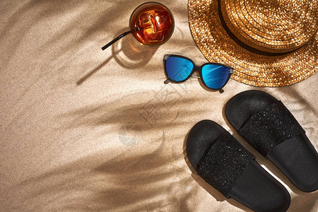 山地草帽和太阳镜都印在沙地背景上棕榈叶的阴图片
