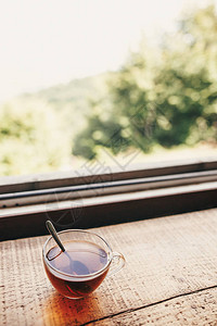 杯热茶在木桌上在窗光与山和天空的景色山顶上的美味饮料夏季旅行和旅行图片