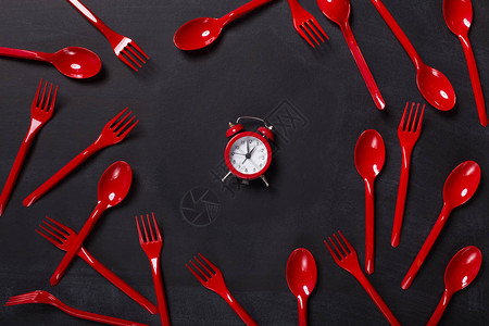 黑背景顶视图的红色面叉和勺子以及小闹钟可移动的餐桌穿戴和图片