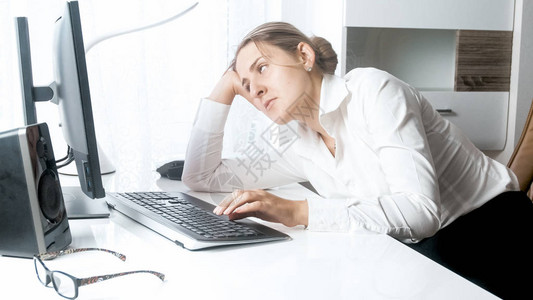 睡眼惺忪的女人看着电脑显示器的肖像图片