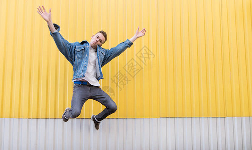 穿着牛仔裤夹克的嬉皮士在黄色明亮的墙壁上跳跃图片