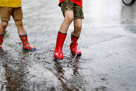 两个穿着红色雨靴的孩子跳进水坑特写孩子们玩得开心泼水夏日大阵雨中背景图片