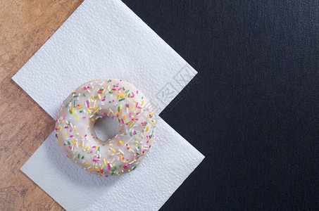 白餐巾上涂有彩色喷洒和霜冻的甜圈位于棕色和黑色石块图片
