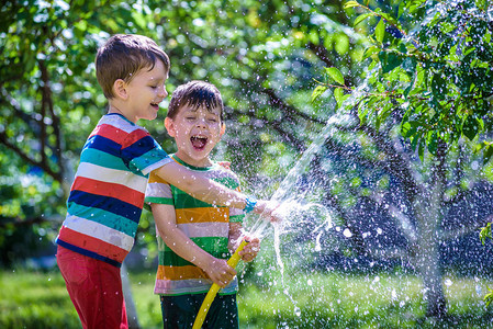可爱的小男孩在花园里用浇水软管浇水图片