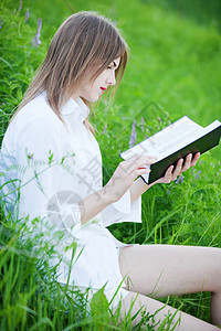 坐在草地上的年轻漂亮女孩穿着白衬衫看斜坡手握着拉克里图片