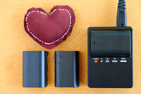 相机锂离子电池用木制桌上的棕色心脏枕头充图片