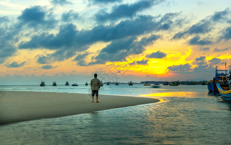 孤独的人在渔村附近的沙滩上观看日落图片
