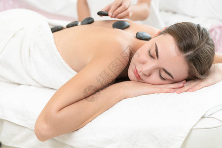 女人在spa沙龙接受专业美容师治疗师的热石按摩治疗豪华健康缓解背部压力和恢背景图片
