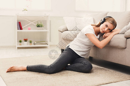年轻悲伤的沉浸在听耳机音乐坐在家里地板上复制空间的年轻女图片