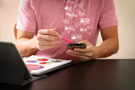 社交媒体和营销虚拟图标屏幕概念穿粉红色T恤衫的商人在现代办公室木制办公桌上与智能电话和数字平板图片