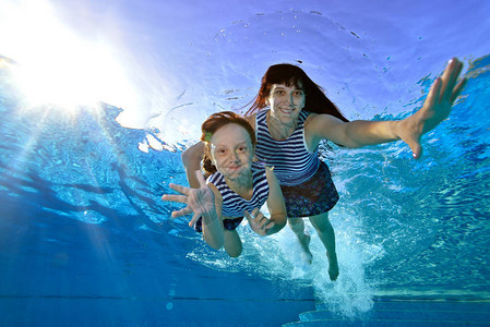 美丽的妈和女儿在蓝色背景的游泳池里游泳他们看着镜头微笑肖像从底部的视图片