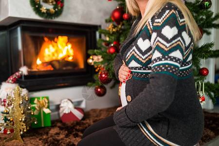 孕妇坐在圣诞树旁边享受节日活动图片