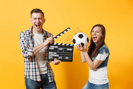 年轻兴奋的夫妇男女球迷用足球电影拍手板和黄色背景隔离的胶片扣板来为支援队欢呼背景图片