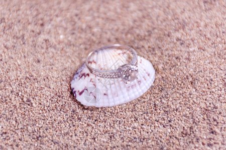 在海壳沙尘模糊和软背景上打钻石订婚戒指珠宝概念关闭图片