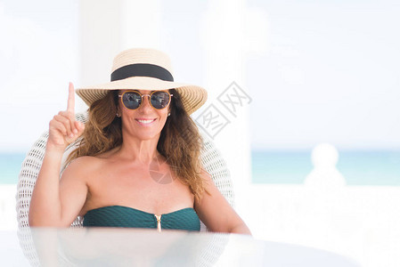 坐在海滩边桌的中年黑发女人惊讶于一个想法或问题与快乐的面孔对图片