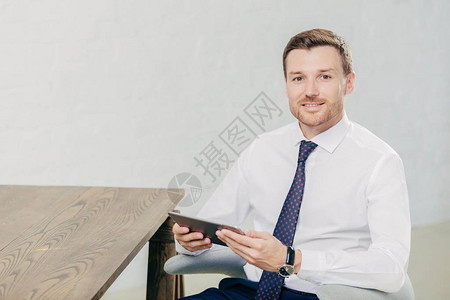 英俊的男自由职业者的室内照片检查现代平板电脑上的通知背景图片