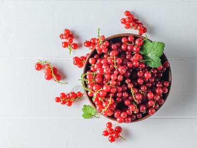 在白木桌上撒了红色的草莓和一碗浆果健康的天然食物的概念图片