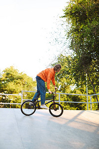 穿着橙色拖车的酷小帅哥骑自行车在现代滑图片