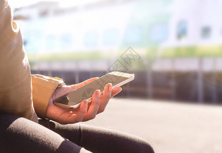 女人在火车站台买票或用手机检查时刻表在模糊的背景下手持智能手机和火车的特写现代背景图片