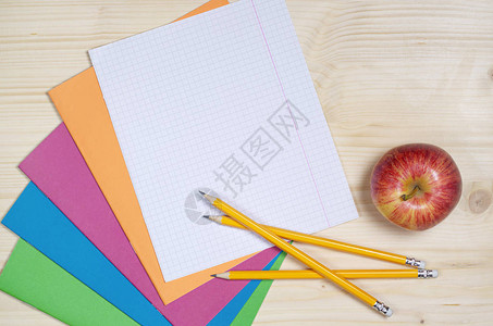 彩色学校笔记本铅笔苹果和木制书桌背景图片