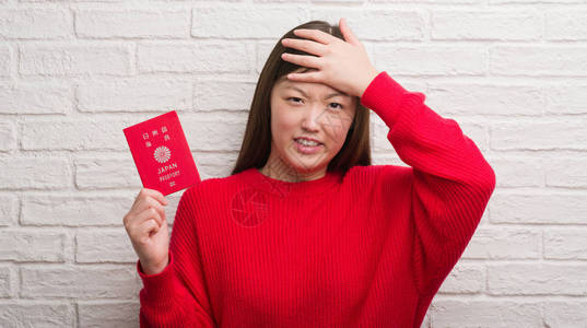 砖墙上拿着日本护照的年轻女子双手捂着头图片