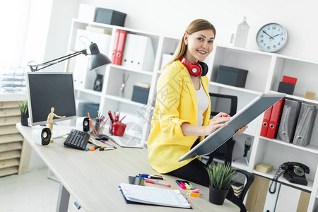 一个穿着白色T恤衫和黄外套的美丽红发年轻女孩正在一间明亮办公室工作照背景图片