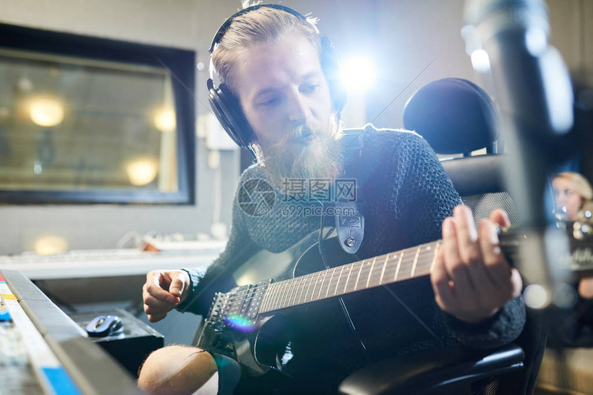 在耳机里自信的人弹吉他和做音乐坐在音响工作图片