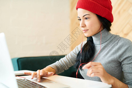现代女青年在咖啡馆从事自由职业和听音乐时使用笔记本电脑图片