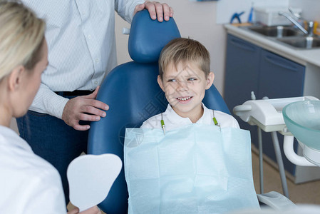 微笑的小男孩坐在牙科椅上听女牙医拿着牙模解释口腔卫生规则的画像背景图片
