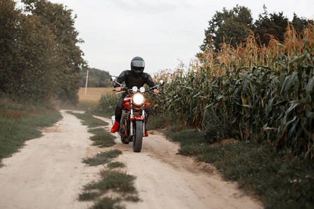 穿着头盔和黑衣的男子乘坐摩托车在玉米田的乡图片