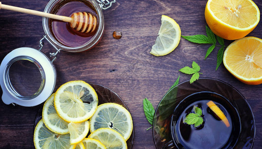 蜂蜜和柠檬木桌上的蜂蜜棒和柠檬片杯子里的茶和罐子里背景图片